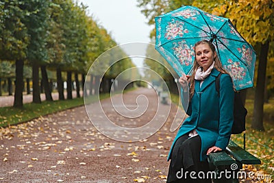 Autumn and walk. A blond woman sitting with umbrella in the Park on a bench. Alley with trimmed trees and rain Stock Photo