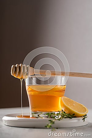 Autumn and winter traditional drinks. Warming hot tea with lemon, honey and thyme. Honey drips down the spoon Stock Photo