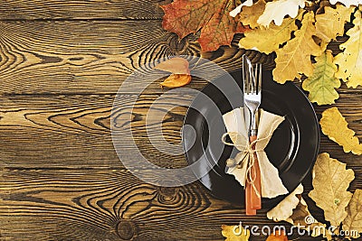 Autumnal table setting for Thanksgiving dinner. Empty plate, cutlery, colored leaves on wooden table. Fall food concept. Stock Photo