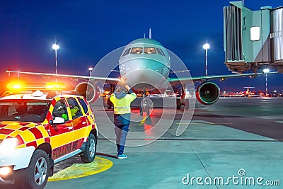 Aviation marshall supervisor meets passenger airplane at the airport at night view. Aircraft is taxiing to the parking place. Editorial Stock Photo