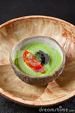 Avocado cream with minced tomato and caviar. Guacamole sauce in handmade ceramic bowl. Modern food - avocado dip. Healthy Stock Photo