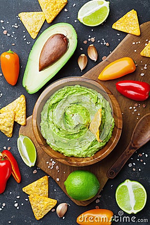 Avocado guacamole with ingredients pepper, lime and nachos on black table top view. Traditional mexican food. Stock Photo