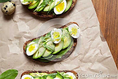 Avocado sandwich toast on dark rye bread made with fresh sliced avocados with spinach, guacamole, arugula and quail eggs Stock Photo