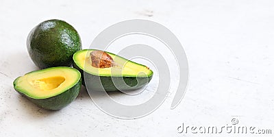 Avocados, one whole, other cut in half, seed visible on white board. Wide banner with space for text on right side Stock Photo