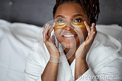 Awakened African Overweight Woman In Bathrobe Solves Under Eyes Facial Problems Applies Patches To Reduce Dark Circles Stock Photo