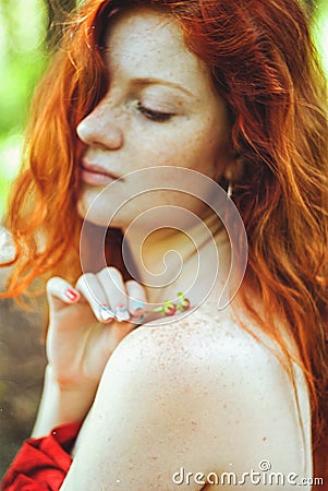 Awesome girl with freckles and red hair posing with a lowered red dress and bare shoulders on wild nature. Stock Photo