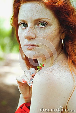 Awesome girl with freckles and red hair posing with a lowered red dress and bare shoulders on wild nature. Stock Photo