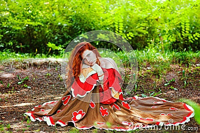 Awesome girl with freckles and red hair posing with a lowered red dress and bare shoulders on wild nature. Stock Photo