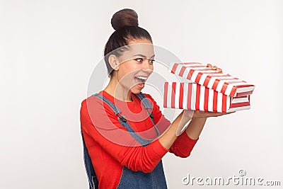 Awesome holiday gift! Portrait of surprised nosy pretty girl with hair bun in denim overalls looking into present box Stock Photo