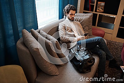 Awesome man in jeans, beige jacket and roll-neck sending e-mail Stock Photo