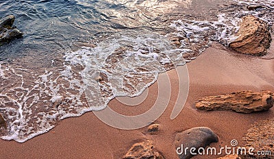 Awesome nature background. Soft beautiful ocean wave on sandy beach with rocks during sunset. Backdrop Stock Photo