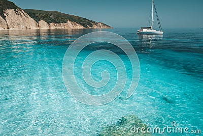 Azure blue lagoon with calm waves and drift sailing catamaran yacht boat. Rocky cliff coastline in background Stock Photo