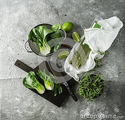 Baby bok choi halves, uncooked green tea noodles, limes, green sprouts on gray background. Top view, square image Stock Photo