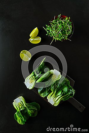 Baby bok choi halves, lime wedges, green sprouts on black background. Top view, vertical orientation Stock Photo