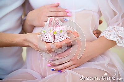 Baby booties for the newborn daughter on a background of a pregnant belly Stock Photo