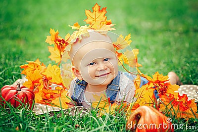 Baby boy with blue eyes in t-shirt and jeans romper lying on grass field meadow in yellow autumn leaves Stock Photo