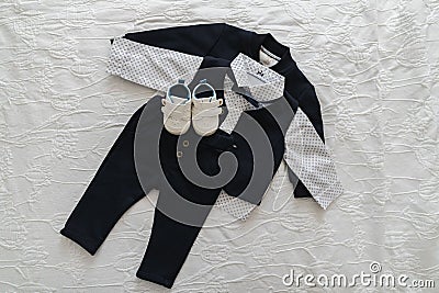 Baby boy clothing on a white sheet of bed with a pair of small shoes Stock Photo
