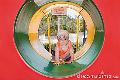 Baby boy crawling with fun through colorful playground tube Stock Photo