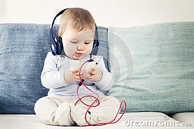 Baby boy listening music at earphones with iphone in hands. Stock Photo