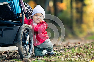 Baby boy playing in autumn forest with stroller, outdoors fun Stock Photo
