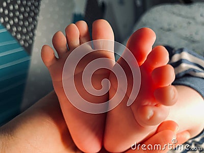 Baby boy small feet, no socks, little toes, playing in bed, blue stripes pijamas Stock Photo