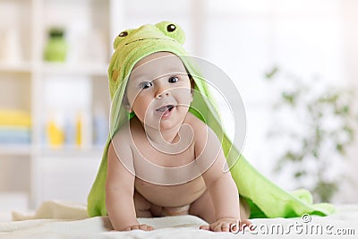 Baby boy wearing green towel in sunny bedroom. Newborn child relaxing after bath or shower. Stock Photo