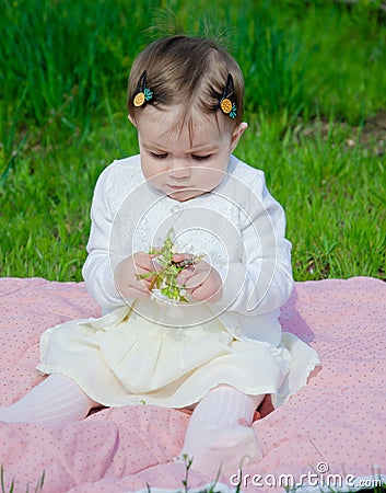 Baby in bright clothes on a pink plaid on green grass in the park Stock Photo