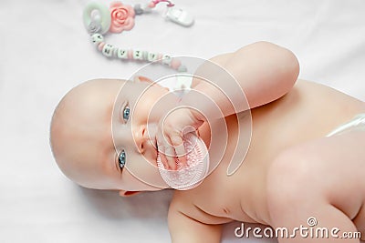 Baby child lying on belly weared with teether in mouth on white background. concept teething babies Stock Photo
