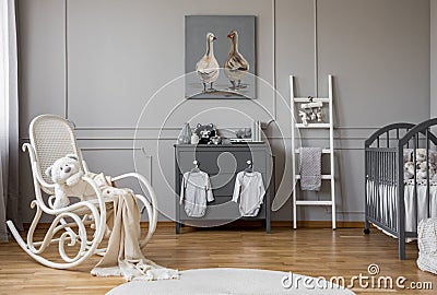 Baby clothes hanging on knobs on grey wooden commode in lovely nursery, copy space and poster on empty wall Stock Photo