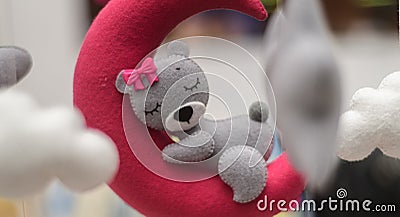 Baby crib mobile ornaments hangings close up shot, grey wool felt bear sleeps on a red plushie moon, surrounded by soft clouds Stock Photo