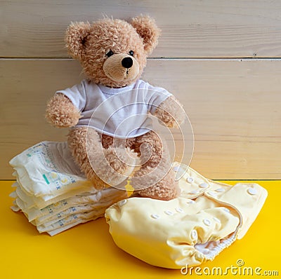 Baby diaper choice concept. Teddy sitting on cloth reusable nappy and disposable diapers Stock Photo