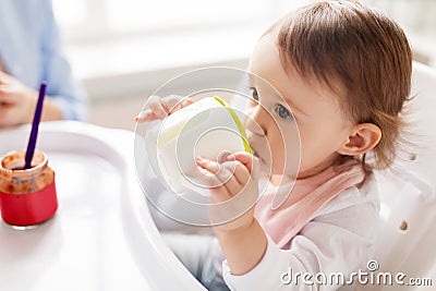 Baby drinking from spout cup in highchair at home Stock Photo