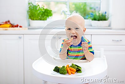 Baby eating vegetables in kitchen. Healthy food. Stock Photo