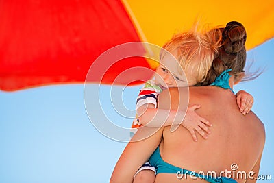 Baby embracing mother on beach under umbrella Stock Photo