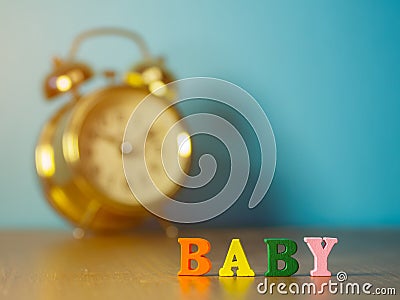 Baby. English alphabet made of wooden letter color. Alphabet baby on wooden table and vintage alarm clock and background is powder Stock Photo