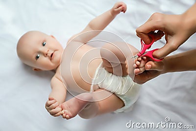 Baby feet close up. Foot and toe pedicure for newborn. Mother cutting toenails for baby with love and care, closeup. Newborn Stock Photo