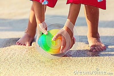 Baby feet walking on sand beach grabbing rugby ball, playful toddler wearing inflatable armbands hand holding ball Stock Photo