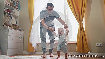baby first steps. daddy a teaches baby toddler son to take first steps. happy family kid dream concept. baby indoors Stock Photo