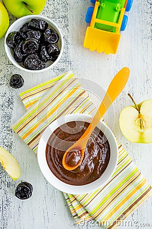 Baby food. Homemade puree of green apples and prunes in a white bowl on a wooden light background. Healhy food. Stock Photo