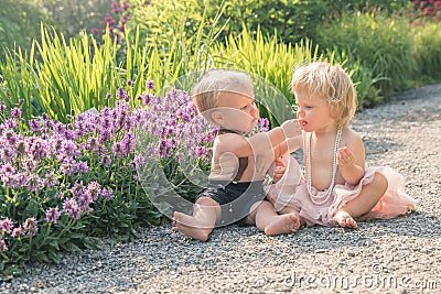 Baby girl and boy sitting in a beautiful garden and pointing to purple flower Stock Photo