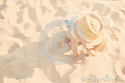 Baby girl child with straw hat and blue dress playing with sand at the beach in summer. Little girl sitting on the shore of the se Stock Photo