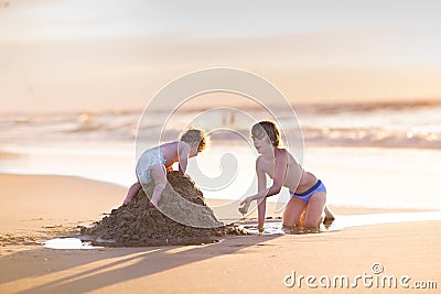 Baby girl climbing sand castle her brother was builded Stock Photo