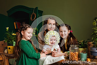 Baby girl in a flower hat on the table with a planting pot and garden plant tools together with her mother and sisters. Home Stock Photo