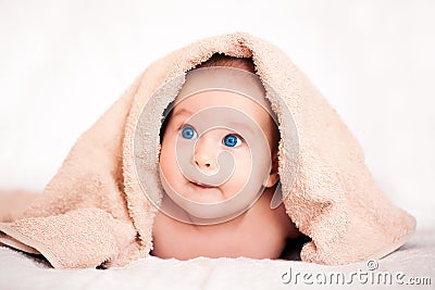 Baby girl is hiding under the beige terry towel Stock Photo