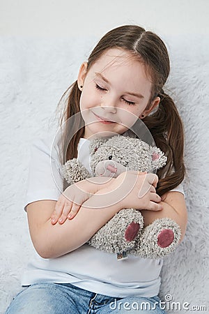 Baby girl hugging plush bear, sitting on a white sofa. Close up Stock Photo