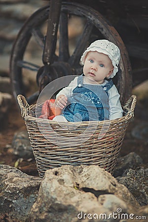 Baby girl with ocean deep blue eyes and pinky cheek wearing white shirt and jeans dress and handmade craft tiny hat sitting in bas Stock Photo