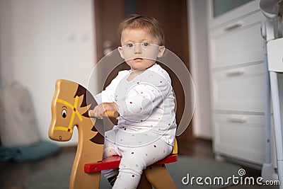 Baby girl playing on wooden rocking horse. Childhood, game at home concept Stock Photo