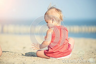 Baby girl in red dress playing on sandy beach near the sea. Stock Photo