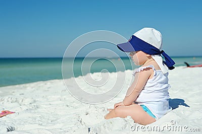 Baby girl sitting on the beach looking at the ocean Stock Photo