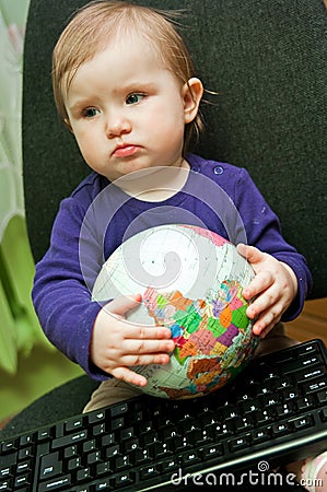 Baby girl sitting with computer keyboard and a globe Stock Photo